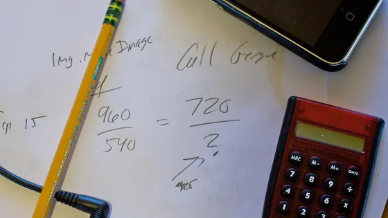 A pocket calculator beside a pencil and a hand-written division sum on a whiteboard