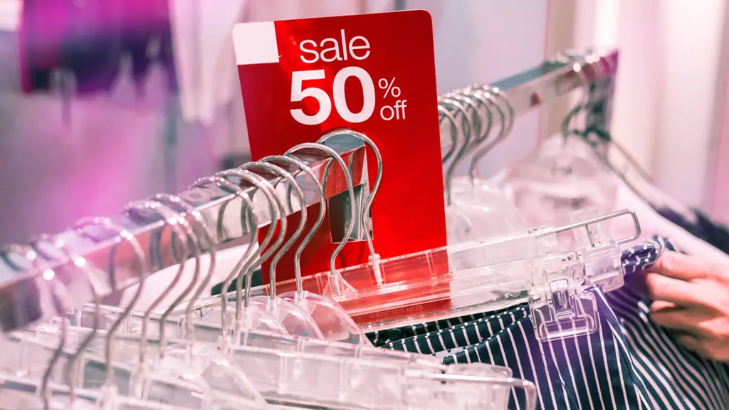 A red fifty percent off sale tag hanging on a rail of clothes in a shop