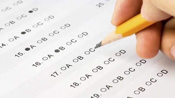 A hand filling in pencil answers on a multiple-choice exam answer sheet
