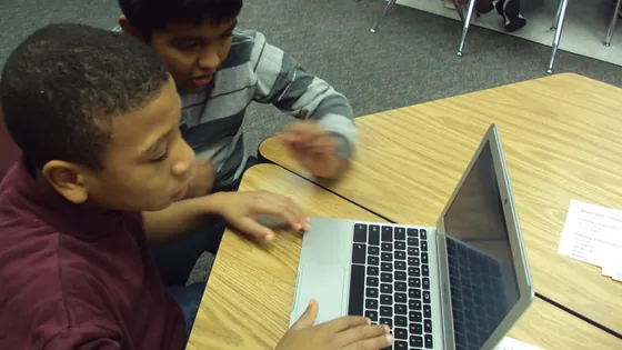 Two school students sharing a laptop at a classroom table